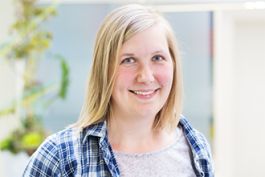 Frau mit schulterlangem blondem Haar, kariertes Hemd, lächelt in die Kamera.