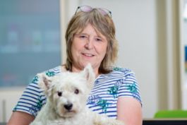 Person mit gestreiftem Shirt, hält kleinen weißen Hund auf dem Schoß, lächelt.