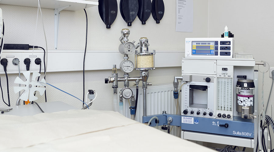 Anästhesiegerät; Bedienfeld mit Anzeige; Druckmesser; Atembeutel; medizinische Schläuche; OP-Tischkante vorne.