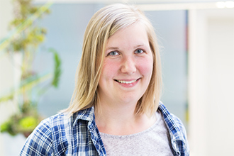 Frau mit schulterlangem blondem Haar, kariertes Hemd, lächelt in die Kamera.